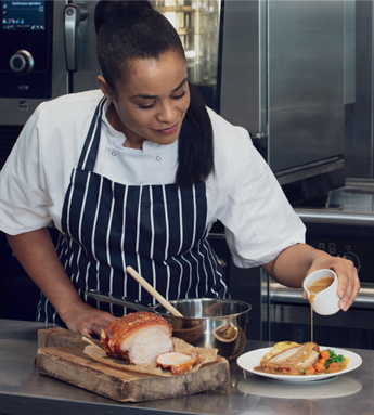 female chef in apron poring gravy onto a roast pork dinner